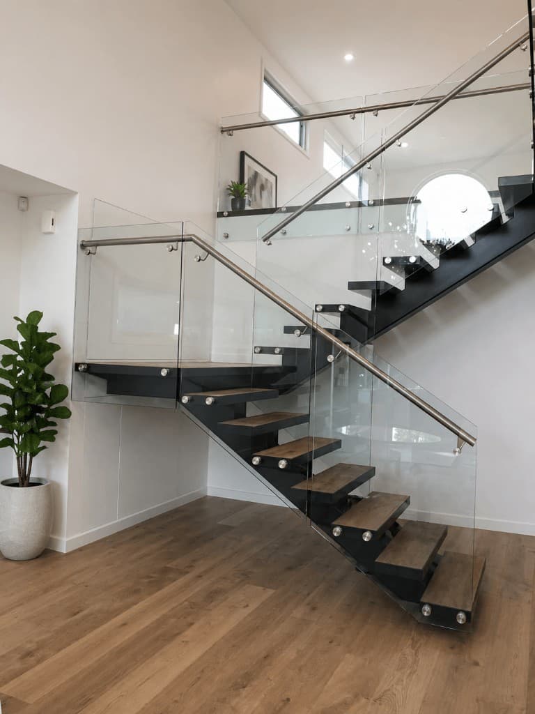 Modern interior staircase with bolt-fixed frameless glass balustrade panels and brushed metal handrail